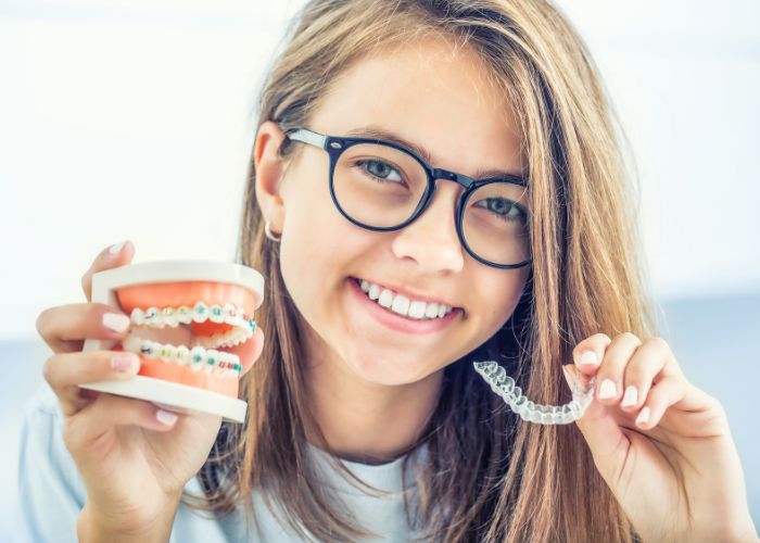 girl holding up Invisalign and colored metal braces side by side