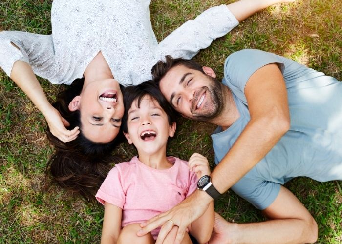 family laying down in grass smiling and laughing